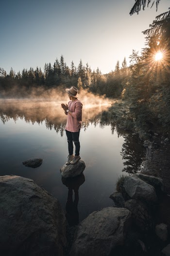 Man in Pink Jacket Standing on Rock Near Lake