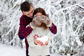 man in red and blue gingham sweatshirt covering eye of girl in gray sweatshirt while holding iceball