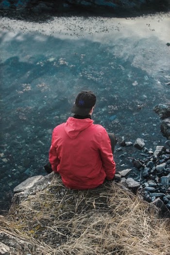 Man in Red Hoodie Sitting on Cliff