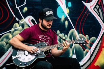 Man in Red Shirt Playing Resonator Guitar Near Wall With Black and Green Painting