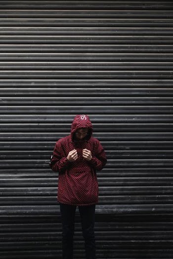 man in red Supreme hooded jacket standing near shutter gate low light photography