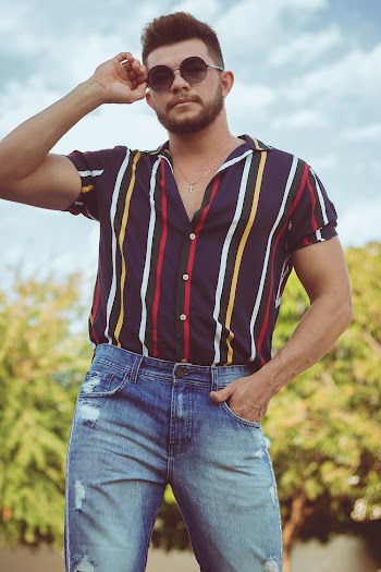 Man in Striped Shirt and Jeans Holding His Sunglasses