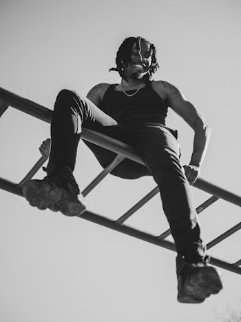 Man in Tank Top Sitting on Top of Monkey Bar