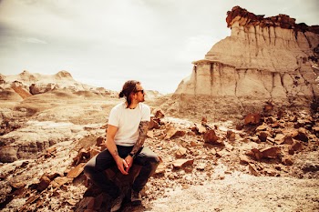 Man in White Crew-neck T-shirt and Black Pants Sitting on Boulder Near Cliff