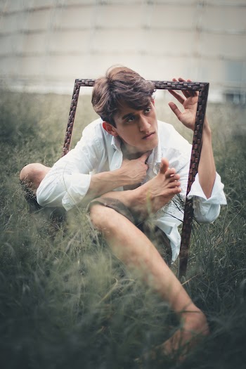 Man in White Dress Shirt Holding Frame Sitting on Green Grass Covered Ground