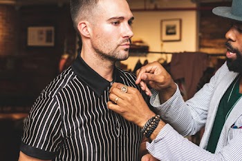 Man in White Pinstriped Suit Jacket Arranging Collar of Man in Black and White Striped Polo Shirt