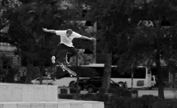 Man in White Shirt and Black Pants Playing Skateboard Near Green Tree during Daytime