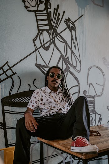 Man in White Shirt and Black Pants Sitting on Table While Leaning on Wall