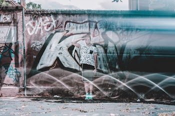 Man in White Shirt and Black Shorts Saluting Graffiti at Daytime
