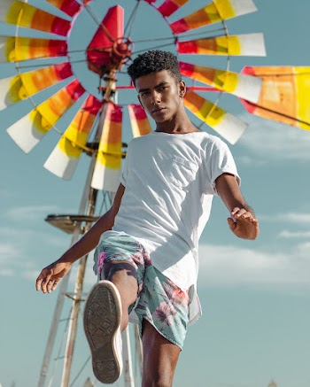 Man in White Shirt Standing Near Yellow, Red and White Wind Mill