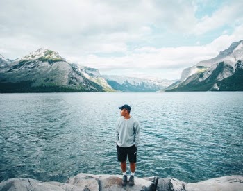 Man in White Shirt Standing on Gray Rock Near Body of Water · Free Stock Photo