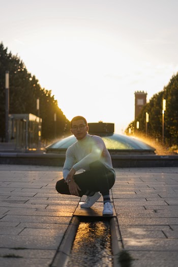 Man in White Sweatshirt Sitting in Front of Water Fountain