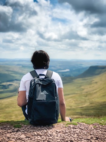 Man in White T-shirt and Black Adidas Backpack Sitting on Green Grass Field