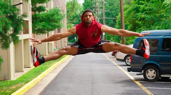 Man Jumping at the Pathway Beside Parking Lot