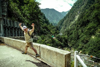 Man Jumping on Concrete Pavement Near Green Mountains Under White Sky