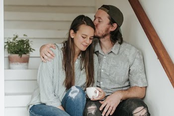 man kissing woman's forehead while sitting on staircase