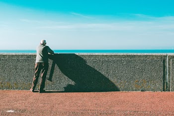 Man Leaning on Gray Concrete Wall Under Blue Sky