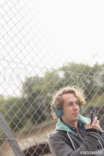 Man listening to music with headphones at chainlink fence