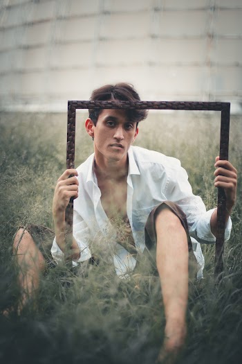 Man Lying on Green Grass Field While Folding Photo Frame