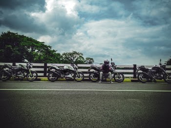Man on Asphalt Road Sitting Beside Sports Bike Under White Clouds Blue Skies Daytime