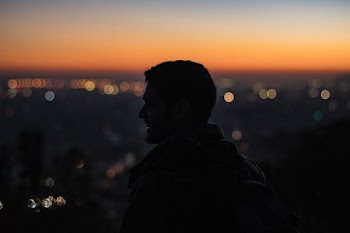 man on high ground facing right looking at city during nighttime