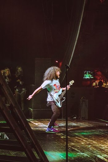 man performing guitar on stage with large black PA speakers