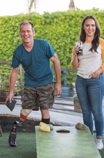 Man Playing Cornhole Beside a Woman Holding a Drink