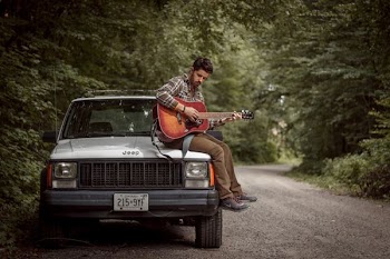 man playing guitar sitting on car