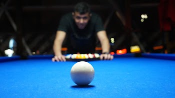 Man Playing Pool Table While Sharply Looking at the White Ball on the Table