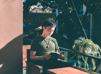 Man Reading Book Near Green Wooden Railing