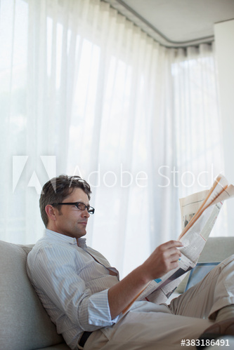 Man reading newspaper on sofa