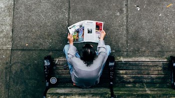man reading newspaper sitting on bench aerial photography