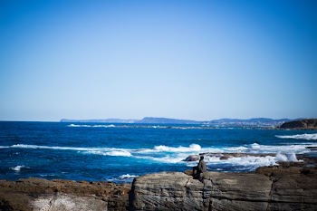 man seats on brown stone near sea during daytime