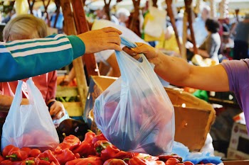 Man shopping vegetables at the market. Farmer vendor hands over plastic bag filled with fresh vegetables to a buyer in CLUJ-NAPOCA, ROMANIA - SEPTEMBER 16, 2017