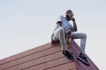 man sit on roof top while holding phone and bottle