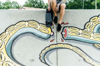 man sitting beside black skateboard