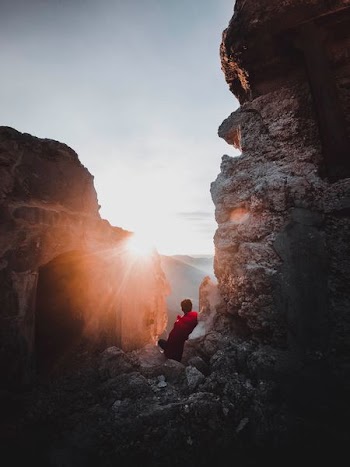 man sitting between rock formation during daytime