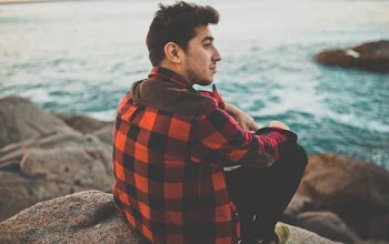 man sitting boulder near body of water