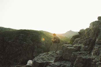 man sitting near cliff during sunrise