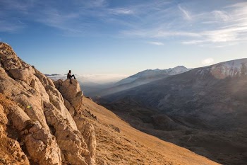 man sitting of brown rock seeing mountains during daytime