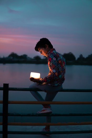 Man Sitting on Black and Yellow Railings Holding White Lighten Bluetooth Speaker