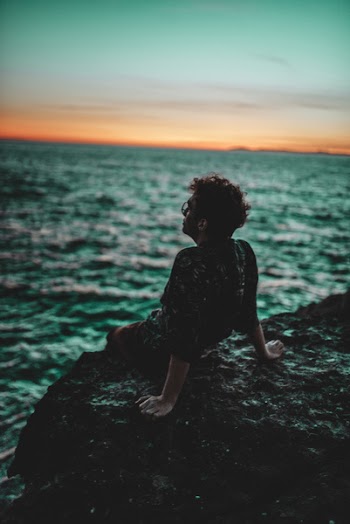 Man Sitting on Black Rock Facing Ocean