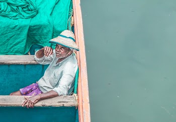Man Sitting on Brown and Blue Wooden Boat Wearing White and Beige Wicker Sunhat