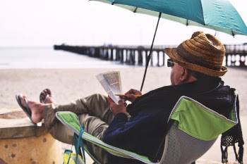 Man Sitting on Chair Under Blue Umbrella Near Beach