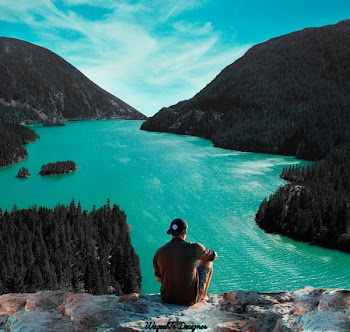 Man Sitting on Cliff in Front of Body of Water