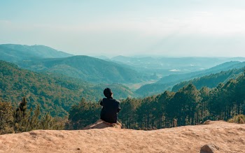 Man Sitting on Cliff Overlooking Mountain