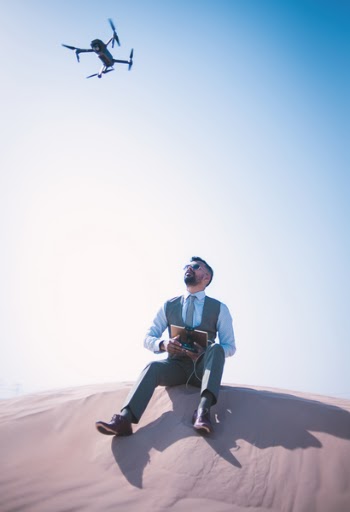 Man Sitting on Desert Ground Looking Up and Operating the Quadcopter