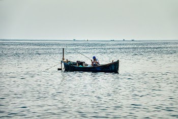 Man Sitting on Fishing Boat on Calm Body of Water