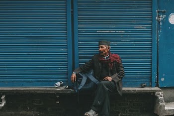 man sitting on gray bench in front of blue shutter door