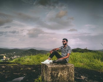 Man Sitting on Gray Concrete Pavement Under Gray Sky